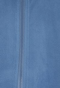 Tessuto in pile blu con superficie testurizzata, dotato di una chiusura centrale con zip. Il materiale è morbido e leggero.