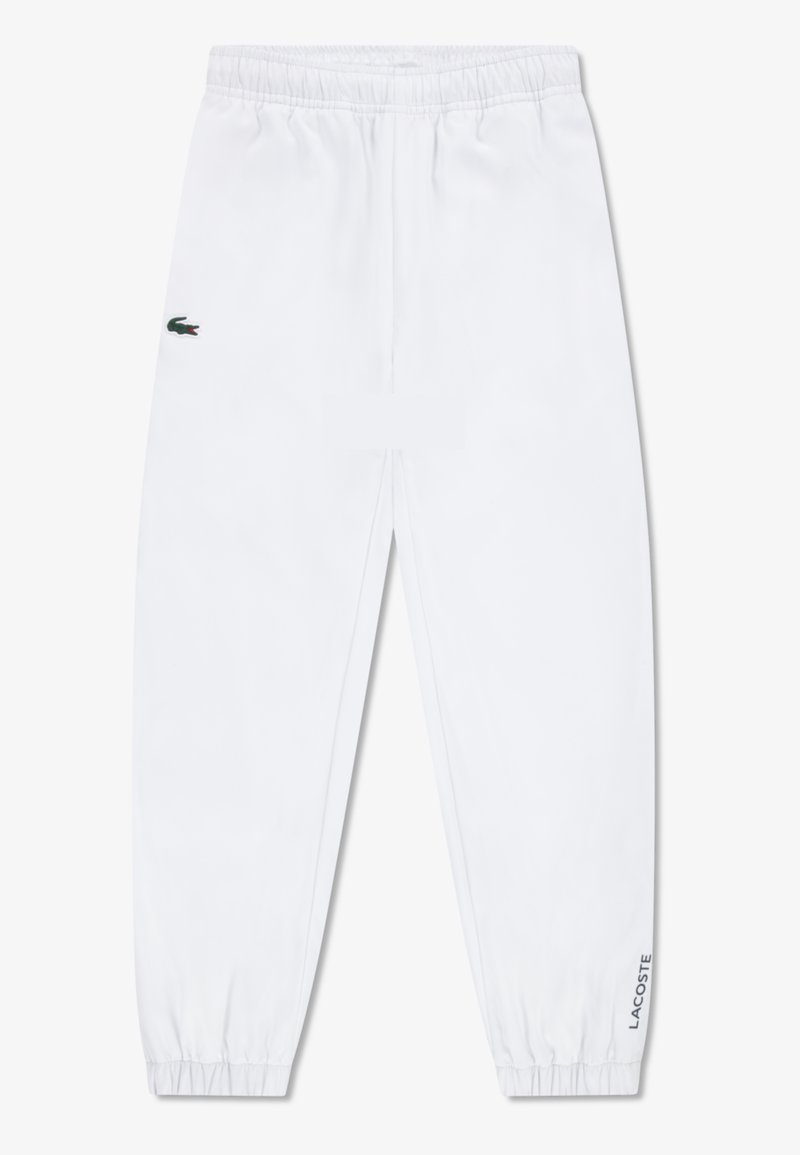 Bijele trenirke s elastičnim pojasom i manšetama, s zelenim Lacoste krokodilskim logotipom na lijevom bedru i natpisom "Lacoste" na desnoj strani.