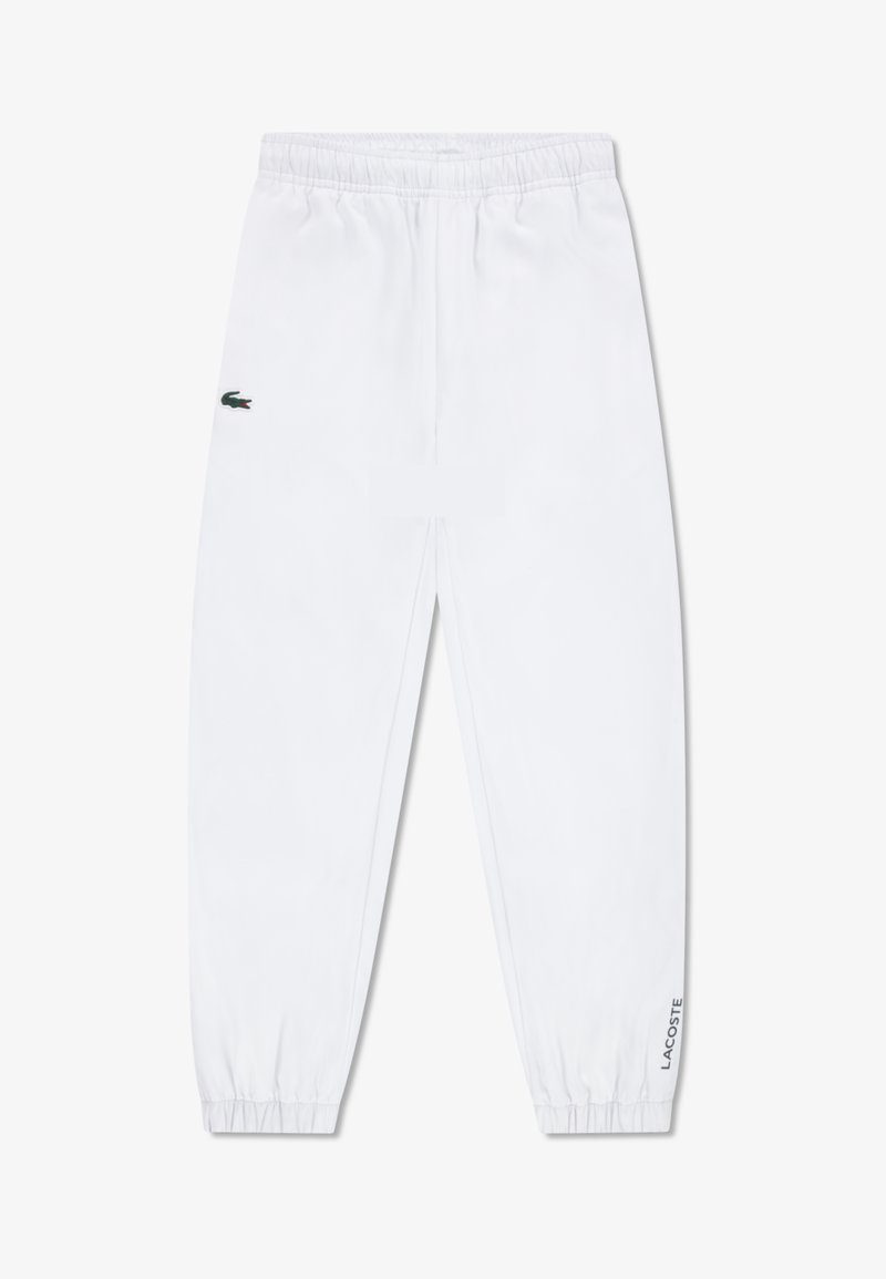 Bijele trenirke s elastičnim pojasom i manšetama, s zelenim Lacoste krokodilskim logotipom na lijevom bedru i natpisom "Lacoste" na desnoj strani.