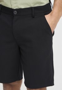 Shorts noirs avec une texture lisse, dotés d'une taille classique, de poches avant et d'une coupe ajustée, adaptés pour un usage décontracté.
