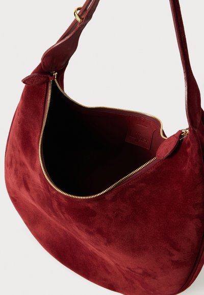 Bordeaux suede schoudertas met een gouden ritssluiting en een soepele, ruime binnenzijde. Kenmerkt zich door een gebogen vorm en een zachte textuur.