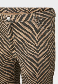 Housut, joissa on seeprahengenvärinen kuvio tan- ja mustalla; valmistettu teksturoidusta kankaasta. Ominaisuuksiin kuuluvat etutaskut ja metallikoristeet vyötärölinjalla.