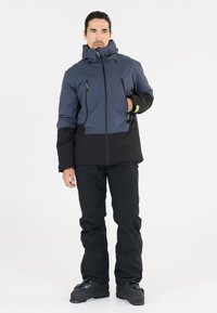 Herrarnas skidjacka i marinblått och svart, med hög krage, fickor med dragkedja och ett vattentätt material. Byxorna är svarta med en slät textur.