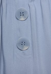 Ljusblått tyg med ett strukturerat mönster, med två runda, genomskinliga knappar med fyra hål, sydda till en rynka.