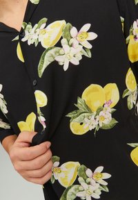 Maglietta nera con stampa di limoni e fiori, con limoni gialli e fiori bianchi, realizzata in un tessuto morbido e con bottoni.