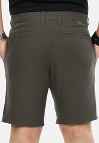 Mann trägt dunkelgraue Shorts mit Gesäßtaschen und Händen in den Seitentaschen, sichtbar von der Taille bis zu den Knien.