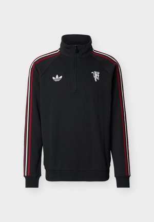 Sudadera deportiva negra con cremallera hasta un cuarto, con rayas rojas y blancas en las mangas, logo de Adidas blanco en el pecho izquierdo y emblema blanco en el pecho derecho.