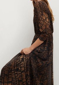 Robe maxi marron à motifs avec texture transparente, manches trois-quarts et taille nouée, présentant un motif géométrique dans des tons plus foncés.