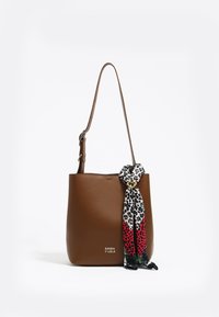 Ruskea nahkainen kassi, jossa on yksi olkahihna ja kuvioitu huivi korostuksena. Edessä on logo ja pinta on sileä.