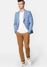 Jasnoniebieski blazer w kratę na białej koszulce, połączony z jasnobrązowymi spodniami i białymi trampkami. Blazer ma klapę w stylu notch.