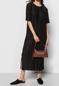 Schwarzes Faltenkleid mit kurzen Ärmeln, seitlichen Schlitzen, kombiniert mit einer braunen Lederhandtasche und schwarzen Slip-on-Schuhen. Glatte Textur, lockere Passform.