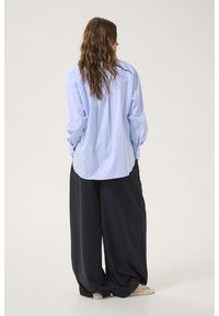 Light blue striped oversized shirt with buttoned cuffs, paired with loose-fitting dark pinstriped trousers. Smooth fabric and relaxed fit.