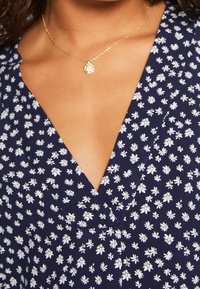 Vestido navy con patrón floral blanco, diseño de escote en V y tejido ligero. Collar dorado con pequeño colgante complementa el atuendo.