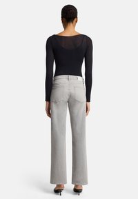 Black long-sleeve bodysuit and high-waisted light grey jeans with wide legs. Model wears black heels and a white belt, shown from the back.