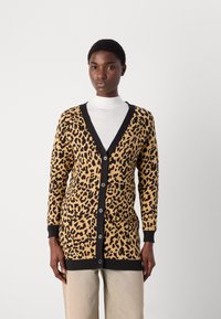 Cardigan s potiskom leoparda v bež in črni barvi, ki ima V-izrez, gumbno zapiranje in rebraste manšete, v kombinaciji z belim puloverjem z visokim ovratnikom.