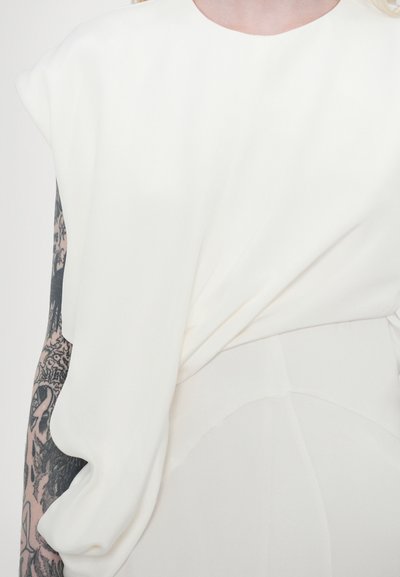 Weißes Oberteil mit weitem, kurzem Ärmel, glatter Textur, asymmetrischem Design und einer subtilen Raffung an der Taille.