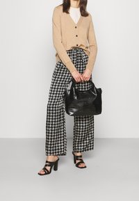 Beige stickad cardigan, mönstrade svarta och vita vida byxor, blanka svarta klacksandaler och en texturerad svart handväska.