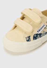 Beige kanvas-sneakers med doble borrelåser, gummisåle og blåmønstret sidepanel med korall-designs.