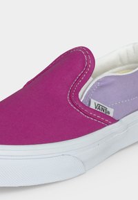 Κοντινό πλάνο ενός παπουτσιού Vans χωρίς κορδόνια με φωτεινό ροζ καμβά στο πάνω μέρος, λευκή σόλα και ανοιχτό μωβ εσωτερική επένδυση με ορατή ετικέτα της μάρκας.