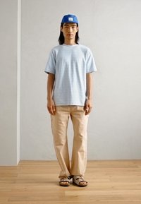 Lys blå tekstureret bomulds t-shirt, beige bomuldsbukser og beige sandaler, sammen med en blå kasket. Enkel, afslappet påklædning.