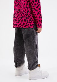 Camisa de manga larga rosa brillante con estampado de leopardo negro, combinada con pantalones vaqueros grises holgados y zapatillas blancas con cuellos acolchados.