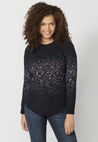 Pulover negru tricotat cu un model colorat și stropit, cu un tiv rotund și mâneci lungi, asortat cu blugi din denim albastru.
