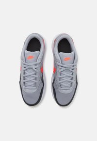 Baskets de sport grises avec des accents rouges, tige en mesh, semelle en caoutchouc, design à lacets et logo en évidence sur la languette.
