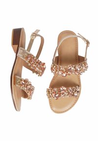 Sandali con cinturini in oro metallico con tacco in legno basso. Decorati con strass rosa e trasparenti sui cinturini. Design piatto e aperto.