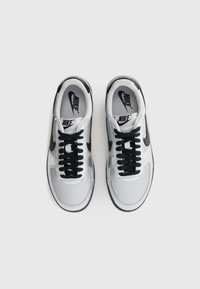 Dvojica bielych a čiernych tenisiek Nike s čiernymi šnúrkami, zobrazené zhora na bielom pozadí.