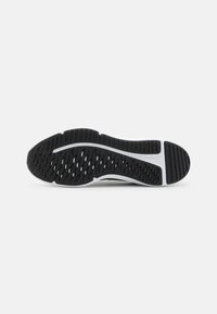 Semelle de chaussure de sport noire avec un caoutchouc texturé et un design de lignes blanches ; dispose de motifs hexagonaux pour une meilleure adhérence et traction.