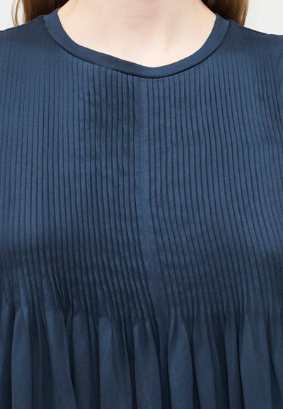 Κοντινό πλάνο ατόμου που φοράει μπλε σκούρο, πλεκτό τοπ με στρογγυλή λαιμόκοψη.