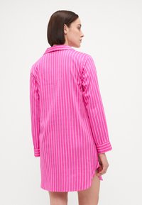 Vestido camisero de rayas rosas con mangas largas, cuello y aberturas laterales. Confeccionado en tela ligera, presenta rayas verticales blancas.