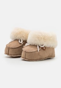 Beige semskede slippers med beige pelskrage, hvite snøringer og brunt skinnaksent. Rund form med quilted tekstur og myk innvendig.