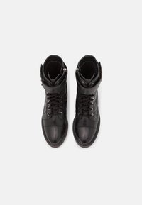 Botas negras de cuero hasta el tobillo con un diseño acolchado, que presentan herrajes metálicos, una correa alrededor del tobillo y un sistema de cordones en la parte frontal.