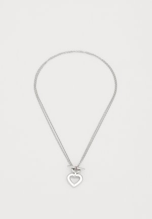 Collar de plata con doble cadena, que presenta un colgante en forma de corazón. El corazón incluye un corte en forma interna y un cierre de palanca.