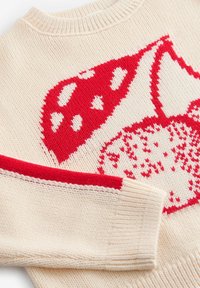Pull crème avec un motif de champignon rouge à pois blancs, col côtelé et accents rouges contrastants sur les manches. Texture tricot doux.