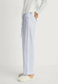 Light blue and white striped pajama pants with a drawstring waist, featuring a straight leg design and soft fabric texture. Plain white top and slippers.