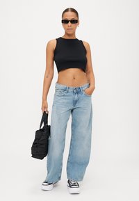 Top cropped preto, jeans de perna larga azul claro e mala preta. Óculos de sol pretos e ténis de plataforma brancos com detalhes pretos.