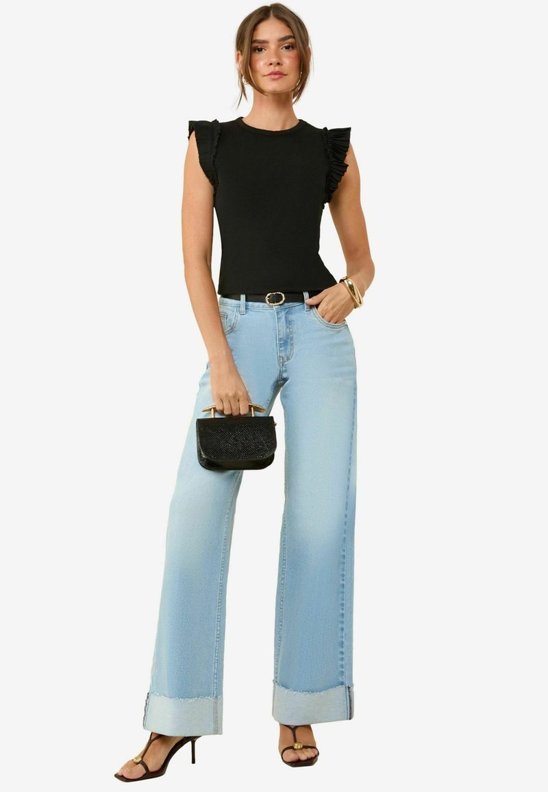 Sort ribbet top med flæseærmer, lyseblå vide jeans med frynset kant, sort håndtaske og sorte stiletter med remme.