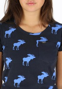 Marine t-shirt met een herhalend patroon van lichtblauwe moose-silhouetten. Ronde hals, korte mouwen, met een klein borstzakje.