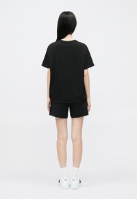 Čierne bavlnené tričko s krátkym rukávom v kombinácii s čiernymi šortkami. Modelka má na sebe biele tenisky a ponožky, zobrazená zozadu.
