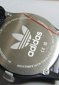 Fond de montre en acier inoxydable avec le logo Adidas, des détails textuels et une bordure rouge. Inclut le numéro de modèle et la classification d'étanchéité.