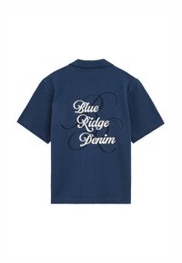Tumesinine lühikeste varrukatega pluus krae ja valge käsitsi kirjutatud tekstiga „Blue Ridge Denim“ seljal, musta peene dekoratiivse spiraaliga üleval.