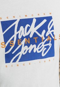 Witte katoenen T-shirt met een blauw rechthoekig grafisch ontwerp met de tekst "Jack & Jones Essentials" in witte en oranje letters.
