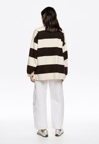 Lange mouw gestreept shirt in room en bruin. Heeft een oversized pasvorm en drop schouders. Gepaard met witte wijde broek en metallic schoenen.