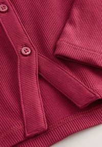 Geribbelde bordeauxrode stof met een knoopsluiting en korte mouwen. Heeft een subtiele textuur en gestikte randen. Geen zichtbare patronen of afbeeldingen.