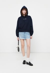 Mørkeblå hettegenser med snor og tekst, parret med en lyseblå denim miniskjørt med slitt kant. Svarte loafers og hvite sokker.