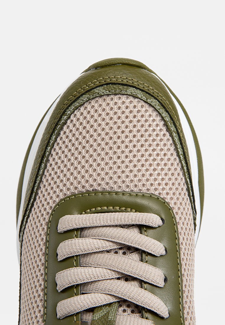 Primo piano di una sneaker a rete beige con rifiniture in pelle verde oliva e lacci beige su sfondo bianco.