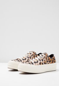 Niskoprofilowe sneakersy z białymi, grubymi gumowymi podeszwami i wierzchem z tkaniny w panterkę, związane białymi sznurowadłami, pokazane obok siebie.