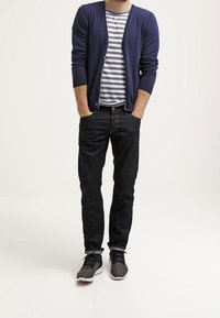 Marinblå cardigan över en randig grå och vit t-shirt, svarta jeans och grå sneakers. Minimalistisk design, åtsittande silhuett, avslappnad stil.